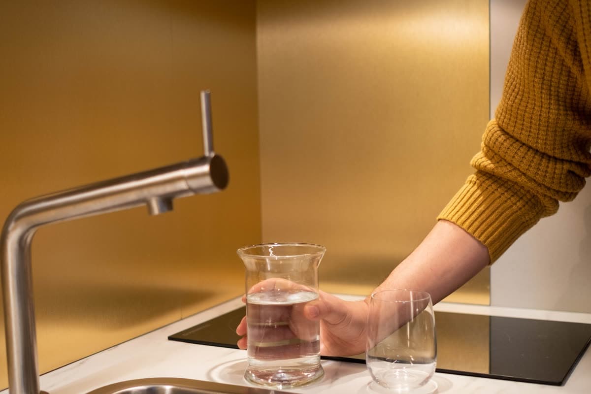 Persona llenando un vaso de agua en el fregadero de una cocina